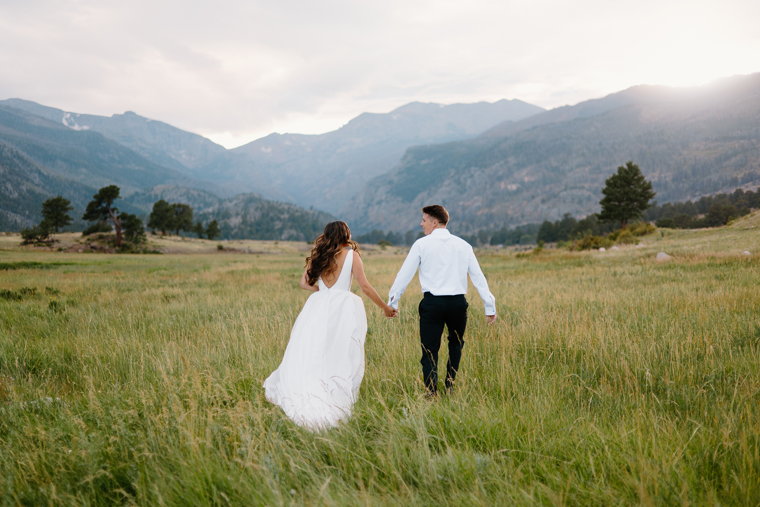 A bride and groom run hand in hand through a scenic Rocky Mountain National Park trail during their adventurous day after session.