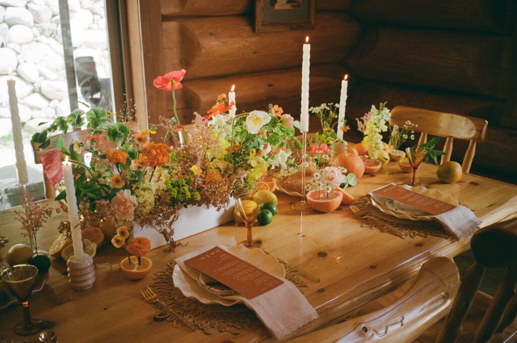 Film photo of a cabin tablescape with oranges, candles, an orange menu, and lush florals inside a rustic log cabin.