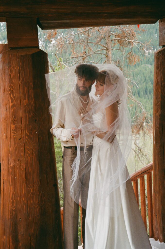 Film portrait of the couple standing together outside the log cabin, posing for a relaxed elopement photo in the Leadville mountains.