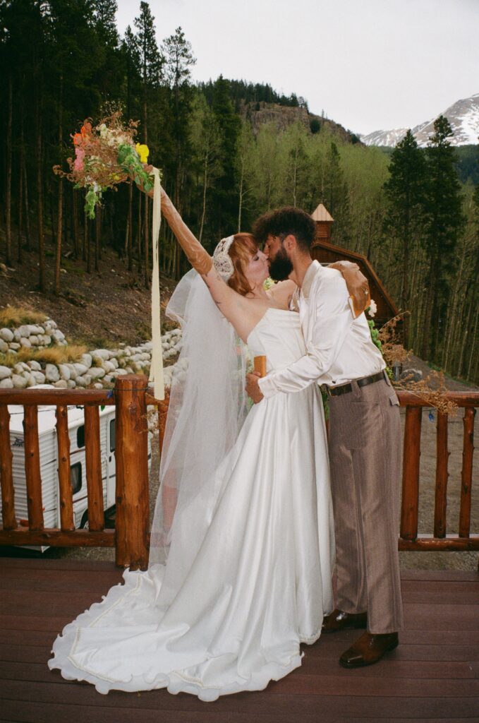 Film photo of the couple kissing outside their Leadville cabin, with the bride holding her bouquet up during their intimate elopement.