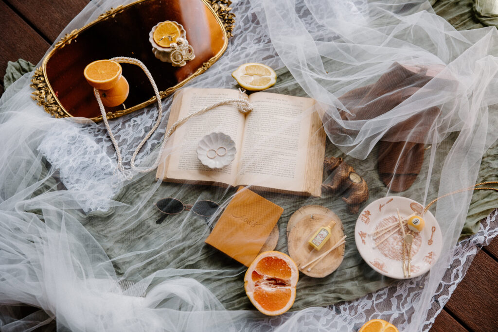 Colorado elopement wedding flatlay with gold rings, oranges, bride’s shoes, and veil arranged on a neutral backdrop.
