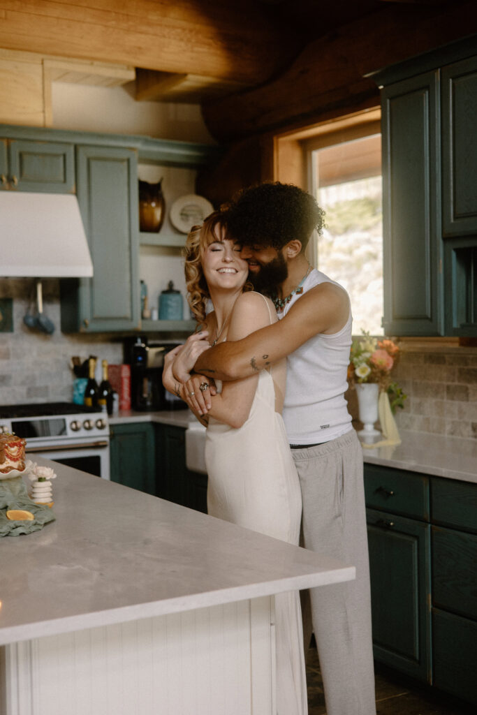 Cozy pre-elopement moment of a couple in pajamas embracing in a rustic Colorado cabin kitchen.