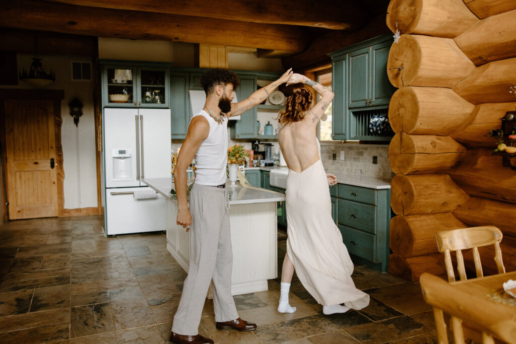 Candid moment of a Colorado elopement couple slow dancing in the warm, rustic cabin kitchen.