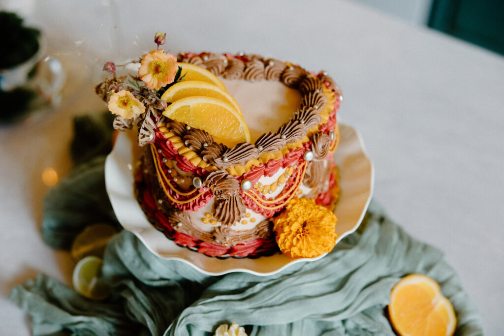 Heart-shaped brown, red, and white cake with orange slices and orange flowers for a Colorado cabin elopement.