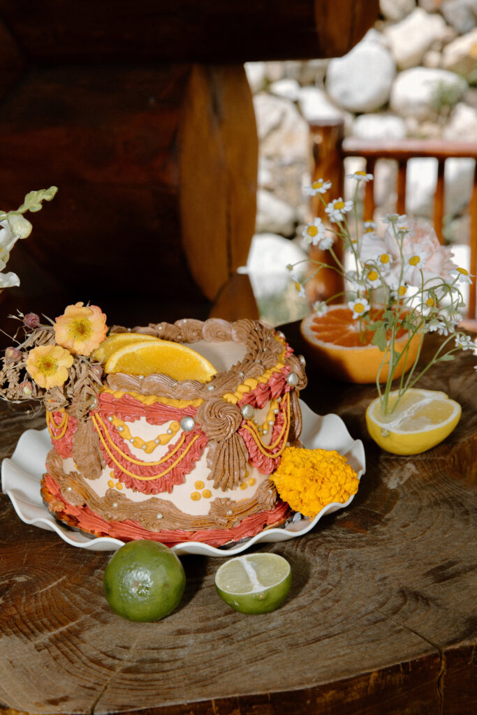 Citrus-accented Colorado cabin elopement cake with orange slices, orange blooms, and a heart-shaped brown, red, and white design.