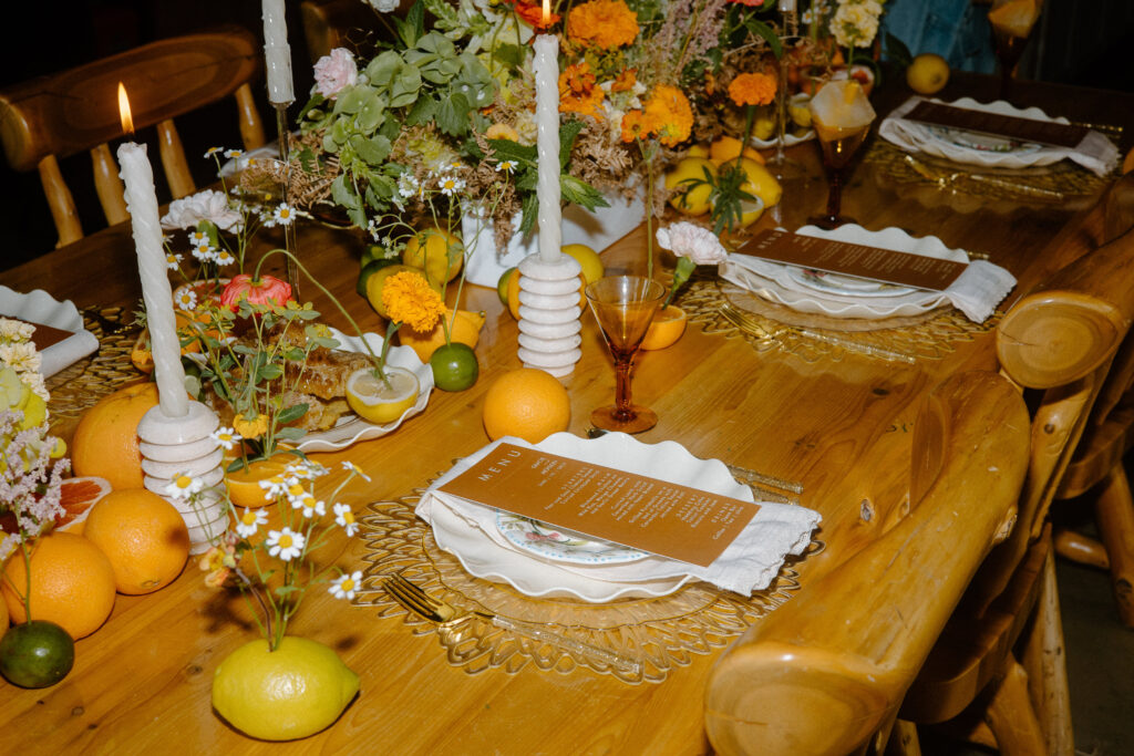 Colorado elopement tablescape with orange menu card, gold flatware, orange goblets, fresh citrus oranges, orange flowers, and white candles.
