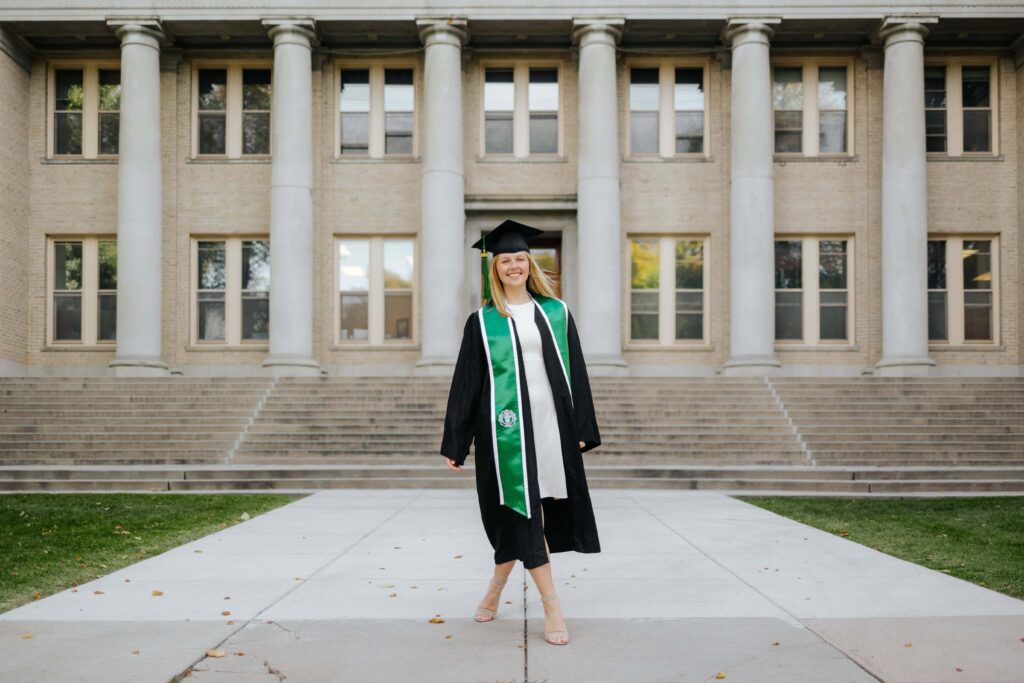 A Colorado State University graduate in a cap and gown posing in front of the histo