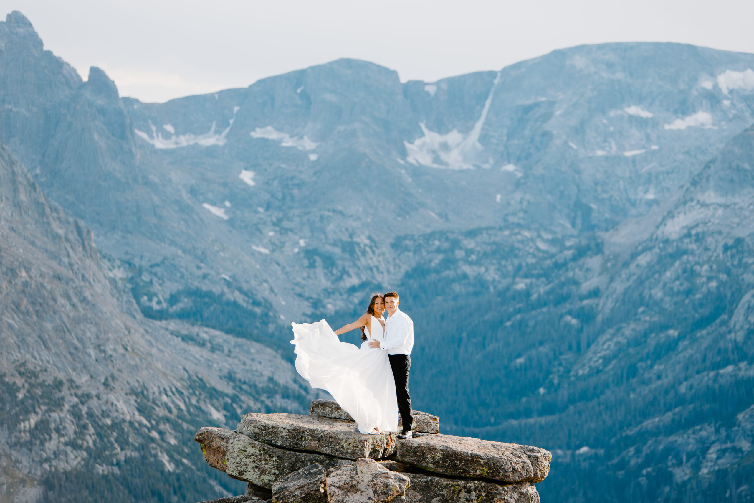 A bride and groom pose for a photo standing on top of a rock on Trail Ridge Road in Rocky Mountain National Park.