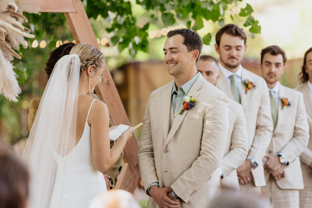 Groom smiles lovingly as the bride says her vows during the ceremony at Lyons Farmette.