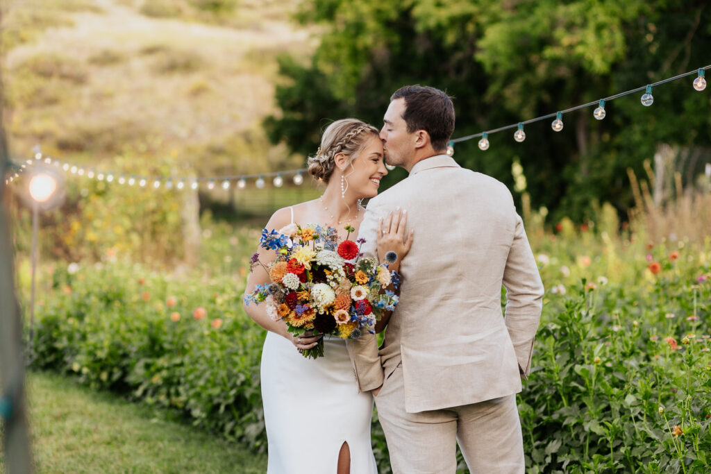 Groom tenderly kisses the bride’s forehead in the picturesque garden at Lyons Farmette.