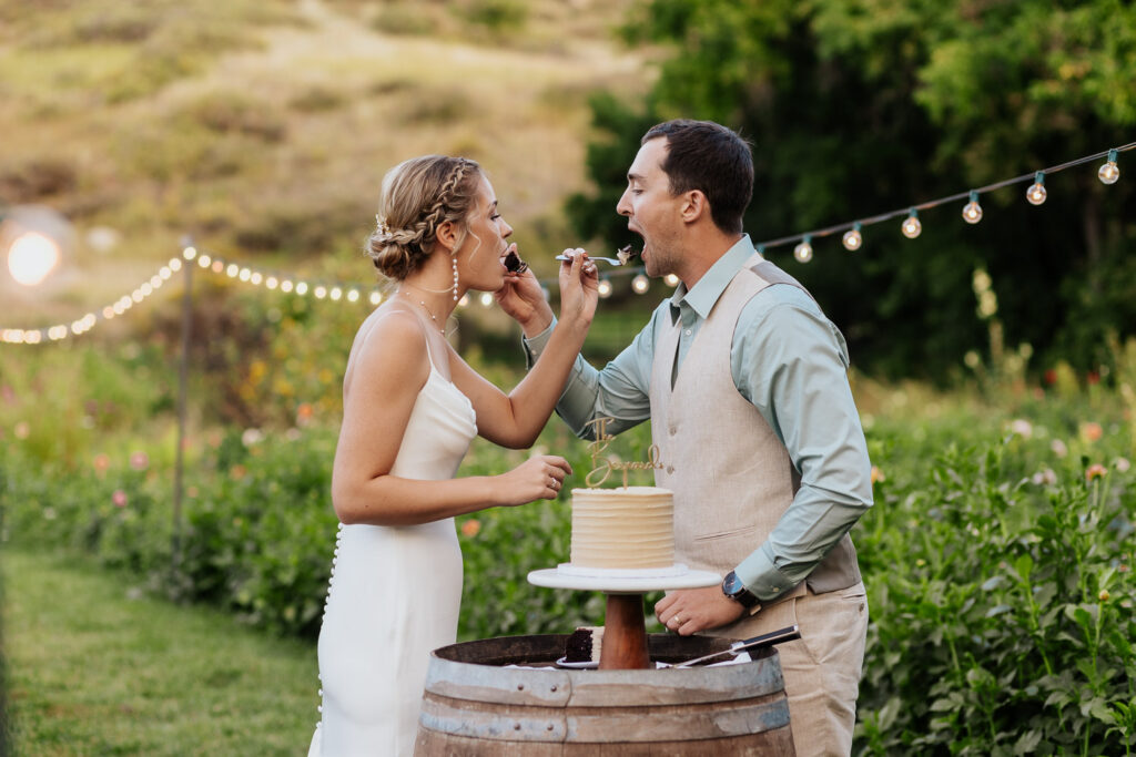 Bride and groom feed each other cake in a beautiful flower garden at their Colorado wedding venue.