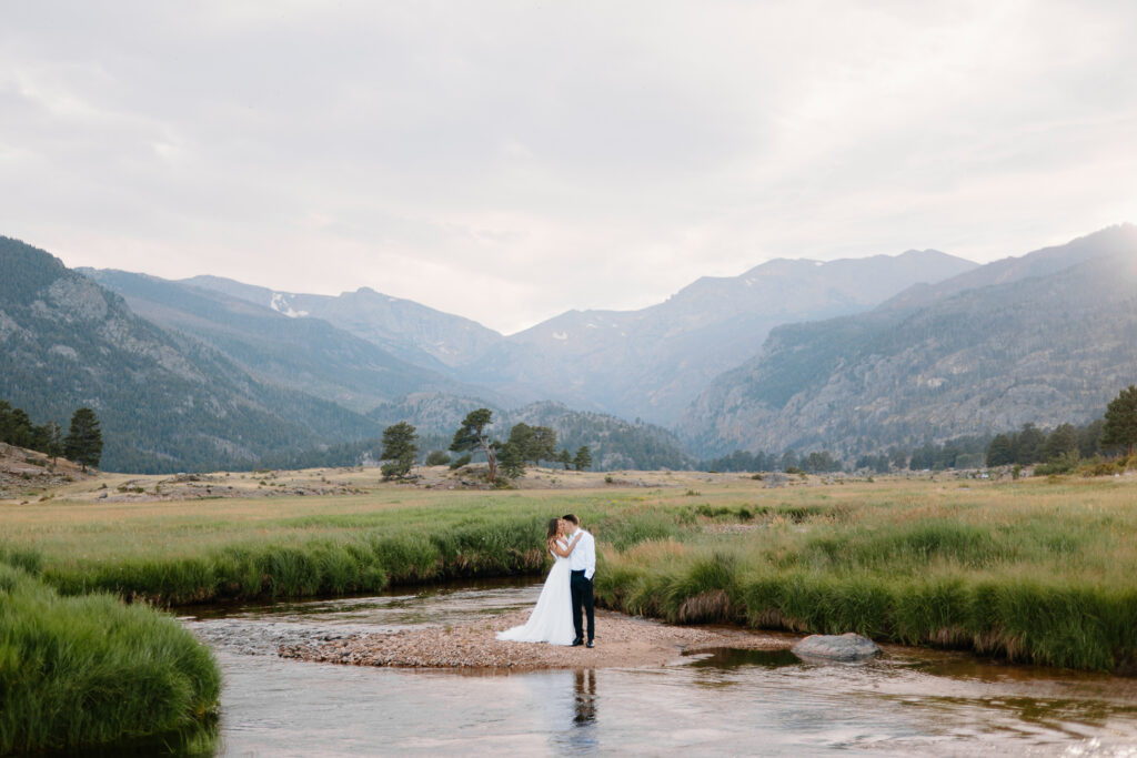 A wide shot of a bride and groom sharing a kiss in the picturesque Moraine Valley, surrounded by the beauty of Rocky Mountain National Park.