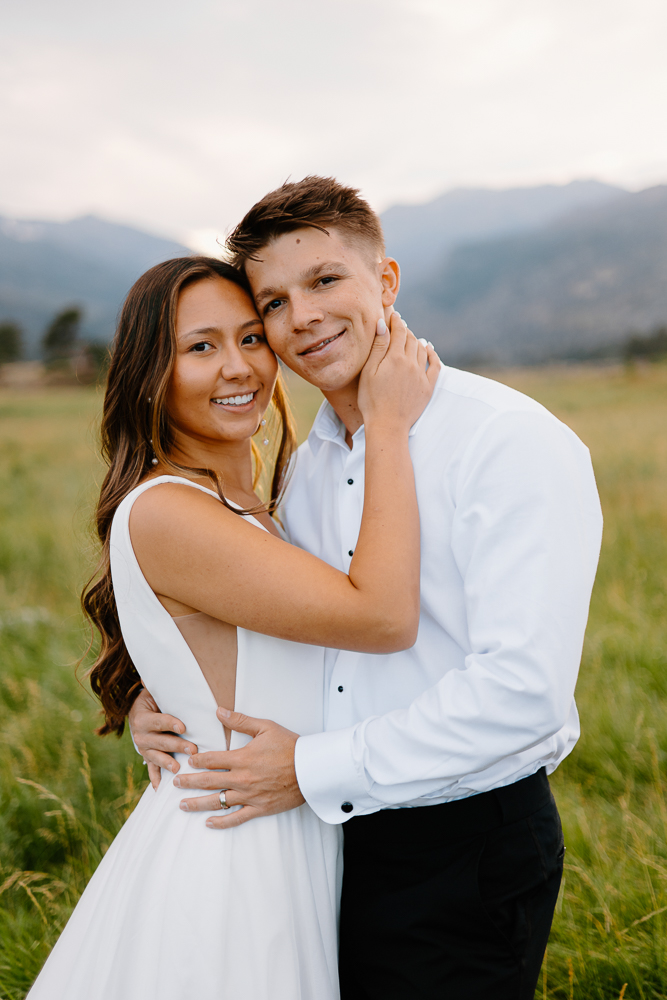 A bride and groom smile directly at the camera with breathtaking Colorado scenery as their backdrop.