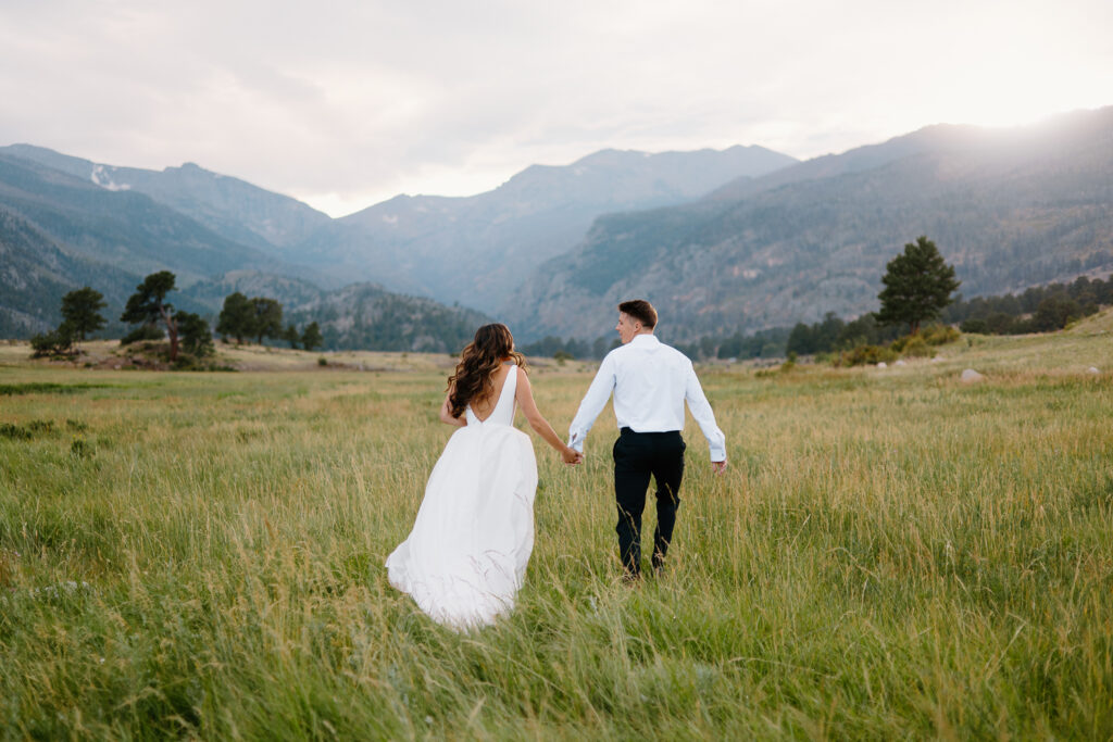 A bride and groom run hand in hand through a scenic Rocky Mountain National Park trail during their adventurous day after session.