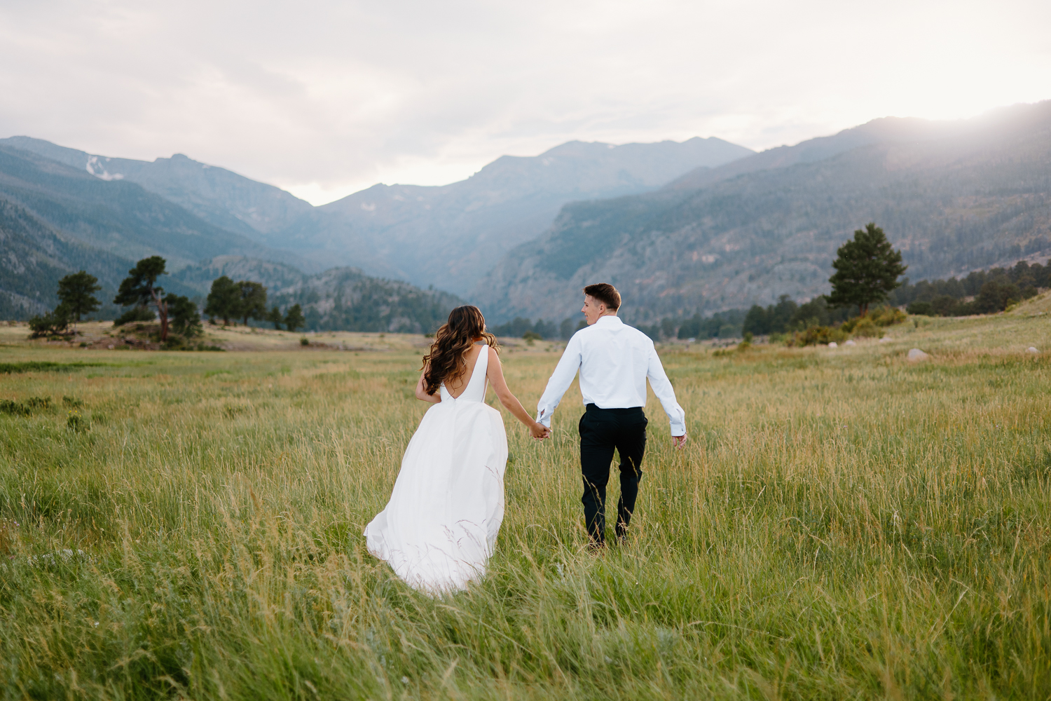 A bride and groom run hand in hand through a scenic Rocky Mountain National Park trail during their adventurous day after session.