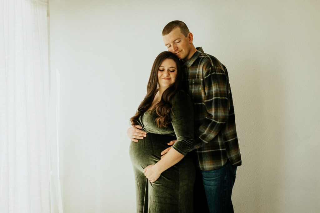 A couple embraces lovingly as they hold her pregnant stomach during their maternity session at Sugarhill Studio.