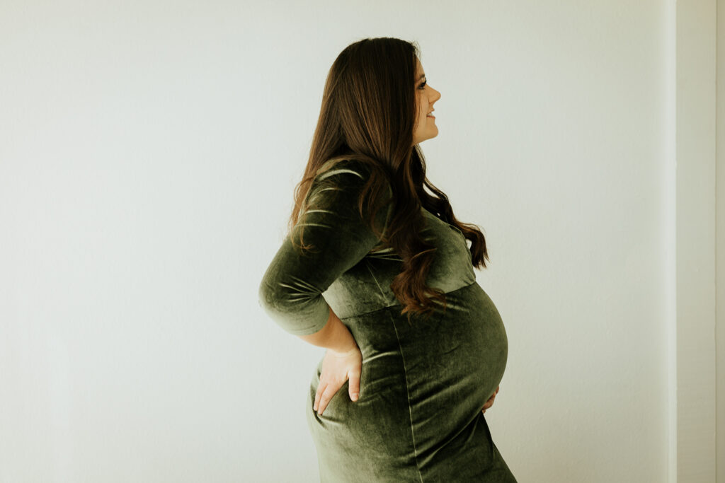 A pregnant woman in a green dress poses gracefully in Sugarhill Studio, showcasing the elegance of her maternity photo session in Longmont, Colorado.