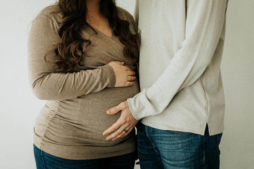 In a close-up maternity photo, the couple embraces while gently holding her stomach.