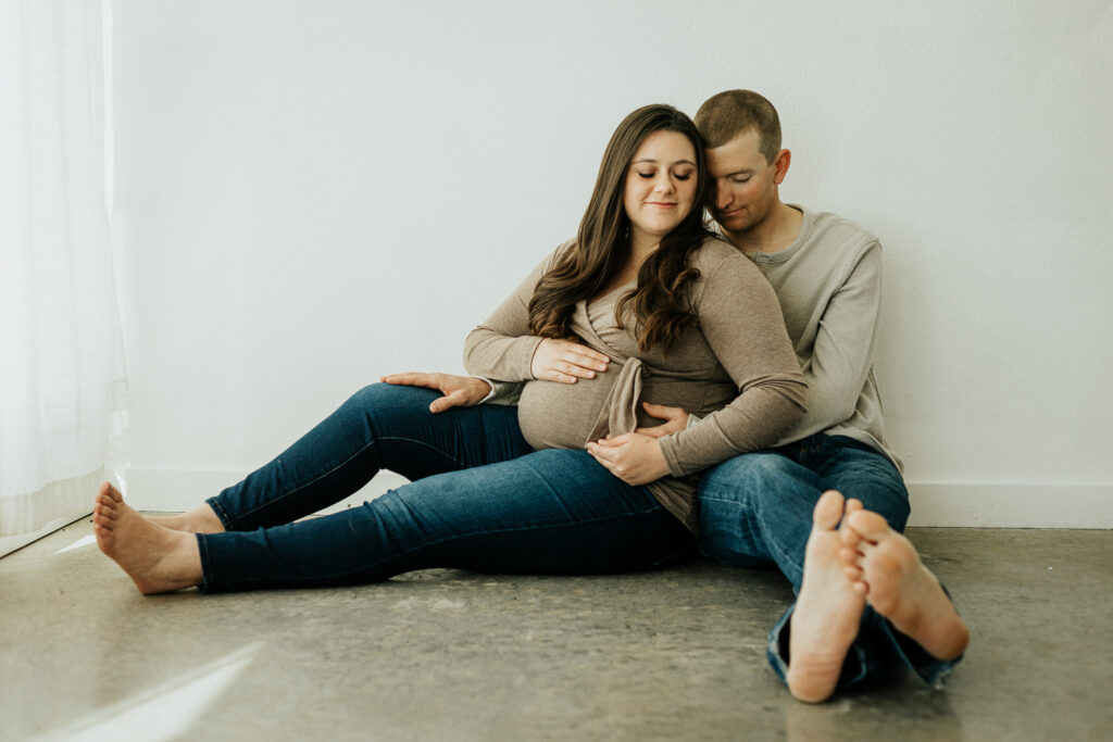 A couple shares a quiet moment sitting on the floor and snuggling during their maternity photo session at Sugarhill Studio in Longmont.