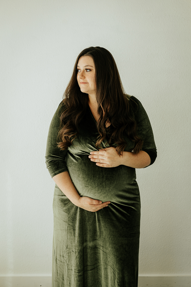 A pregnant woman gently holds her belly during her maternity session at Sugarhill Studio, capturing a tender moment of anticipation.