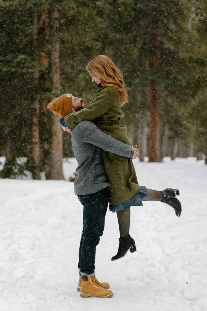 A man lifts up his partner during their engagement photos at Echo Lake, Colorado.