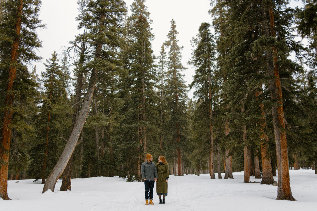 A bride and groom hold hands while standing among trees.