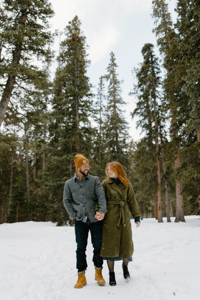 A bride and groom walk happily through the snow.