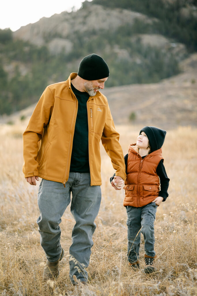 A father holds his sons hand and walks towards the camera while taking Family Photos in Fort Collins, Colorado.