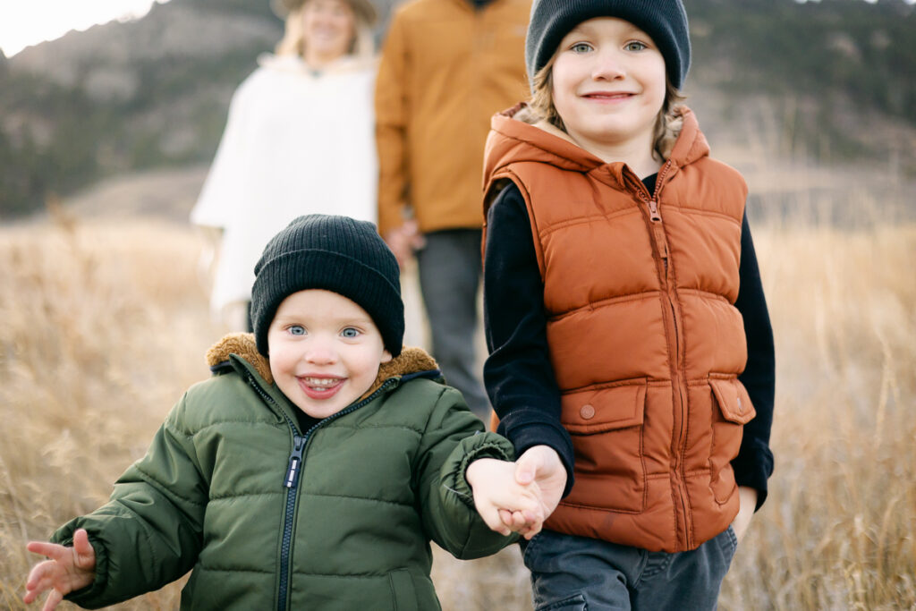 Two brothers hold hands and walk towards the camera while taking Family Photos in Fort Collins, Colorado.